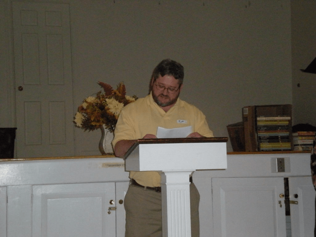 A man with glasses is at a podium in a church space.