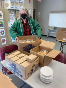 A masked NewBridge CEO Michelle Borden stands surrounded by boxes on a table. 