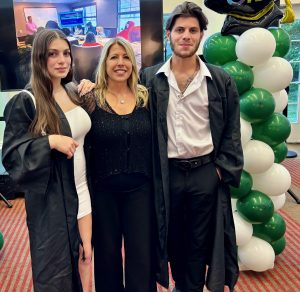A happy mom is pictured between her two adult children, presumably celebrating a graduation with green and white balloons in the background.