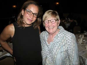 Two women are posed together at a table event, smiling for the camera.
