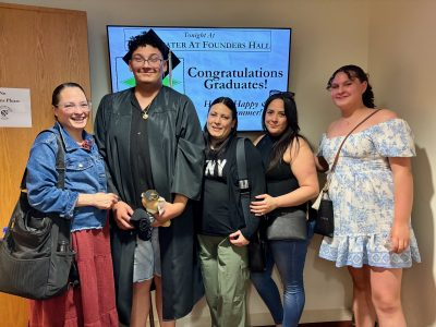 A smiling graduate in a cap and gown poses with family