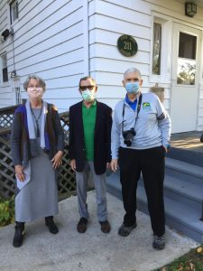 Three masked people stand in front of a building at 211.