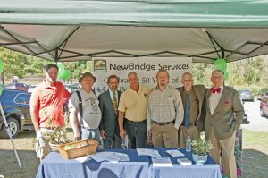 A group of seven people are posed behind a table under a tent