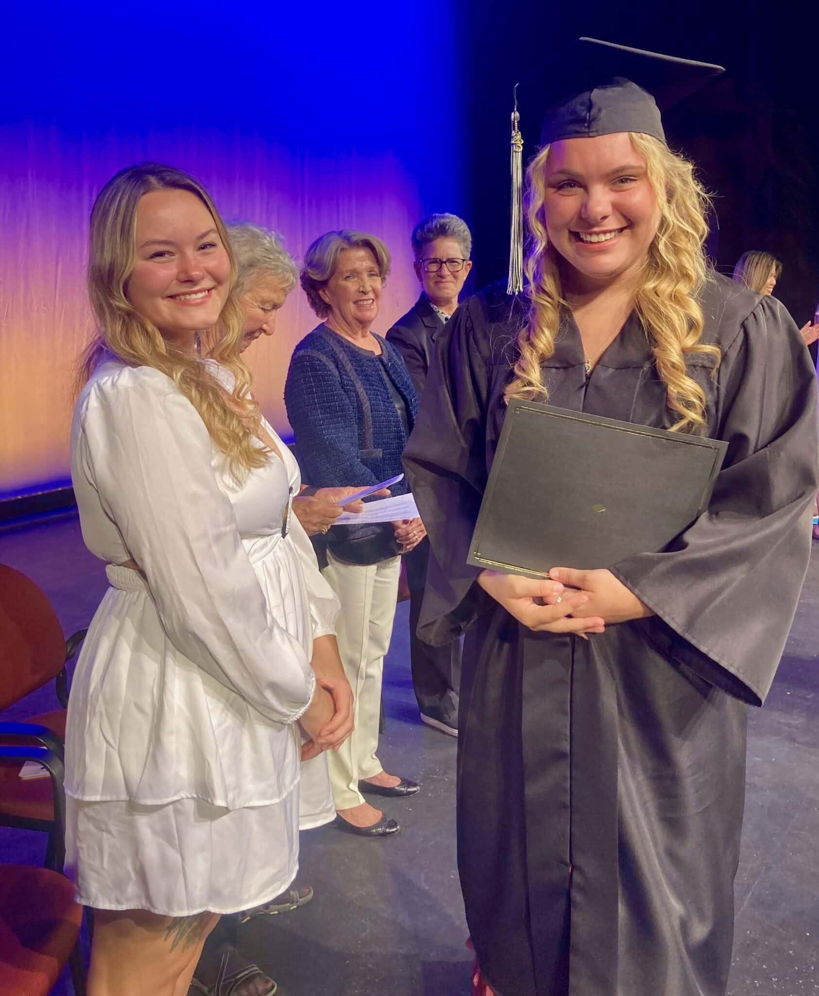 A group of women pose for a graduation photo, with a NewBridge Jobs Plus alumna smiling in her cap and gown. 