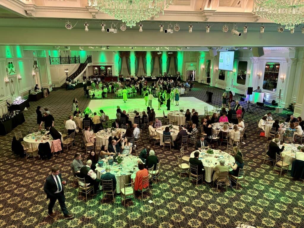 An indoor event has tables and a stage with green lighting.